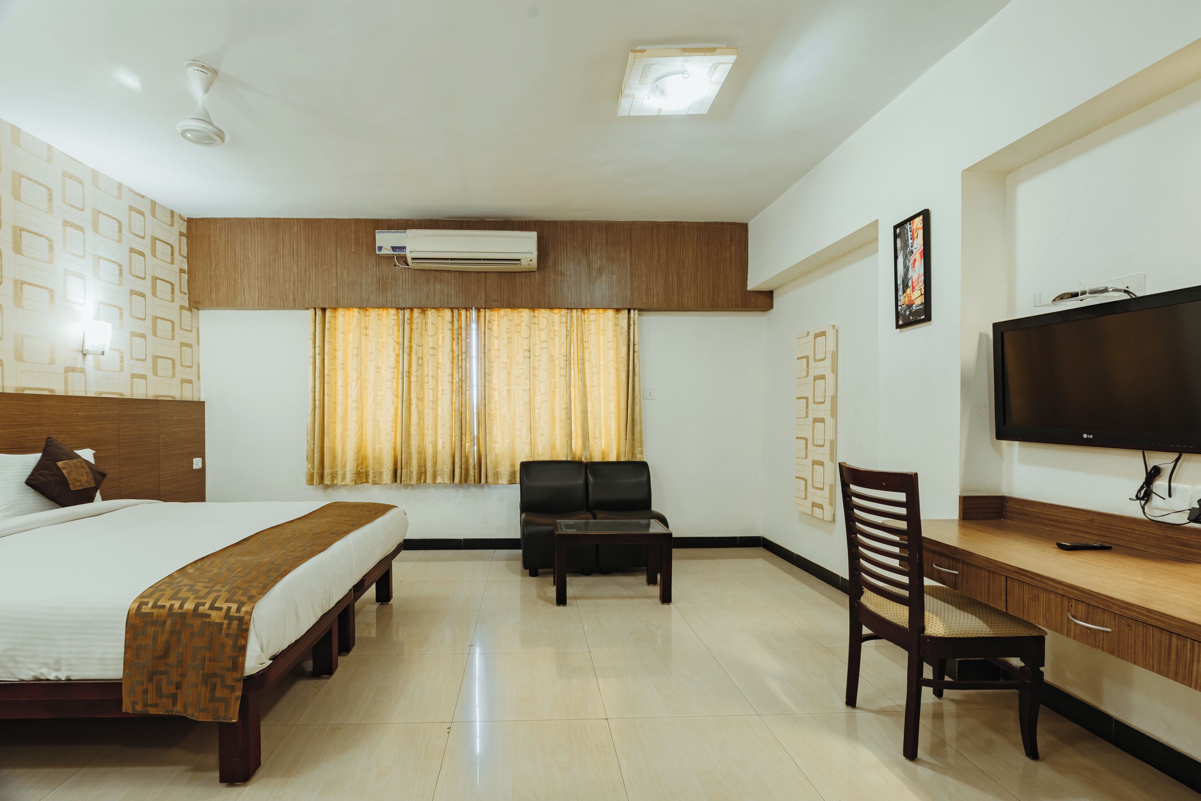 A hotel room with a bed, a desk, a chair, a television, and an air conditioning unit.
