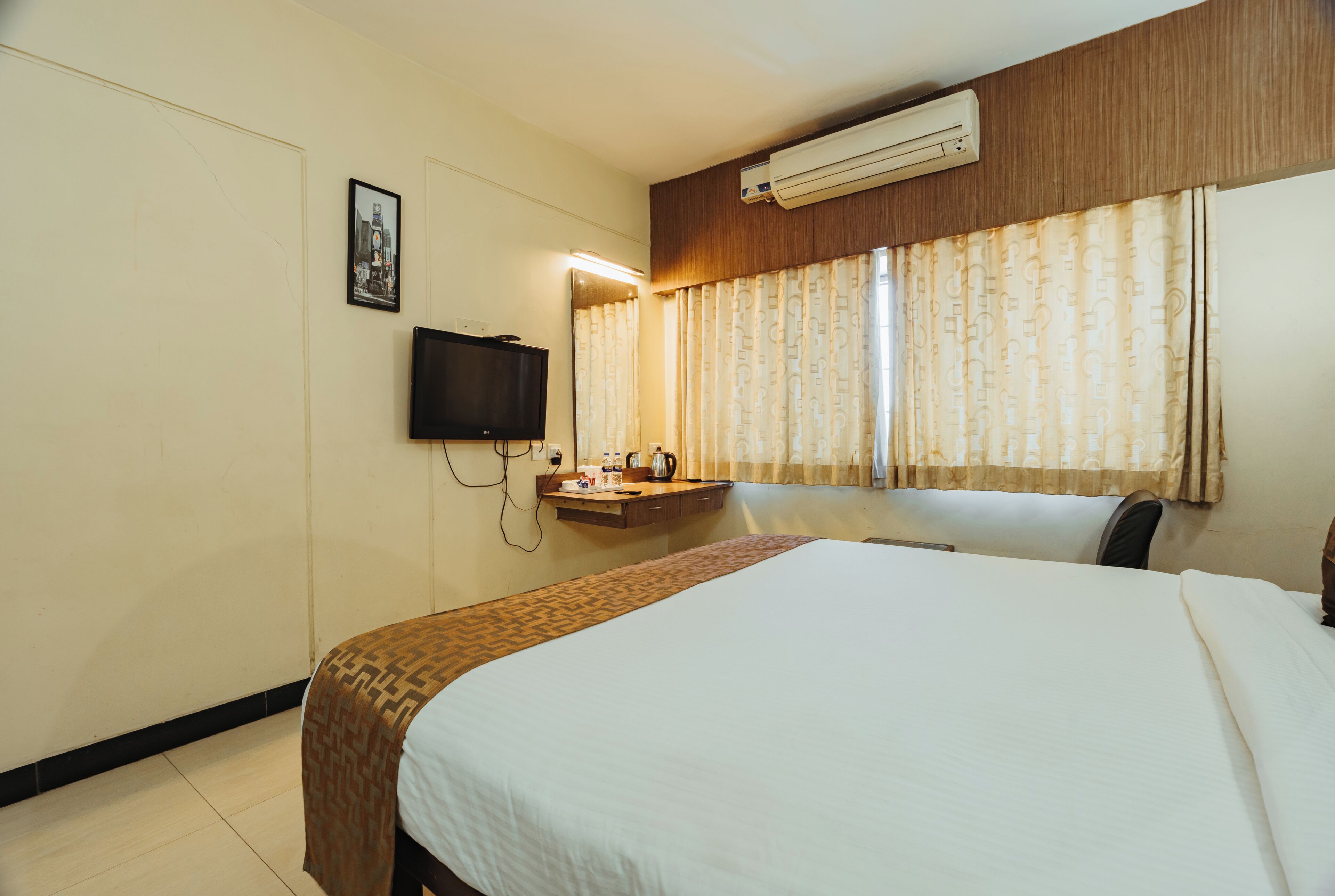 Habitación de hotel con cama, televisor de pantalla plana montado en la pared, mesita de noche y ventana con cortinas.