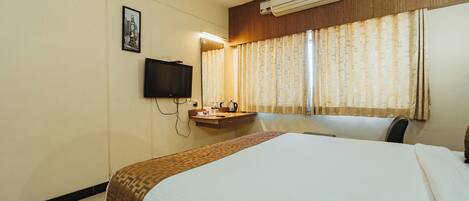 A hotel room with a bed, a flat-screen TV mounted on the wall, a bedside table, and a window with curtains.