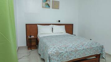 Un dormitorio con estructura de cama de madera, colcha estampada con motivos florales, mesita de noche con teléfono y dos obras de arte colgadas en la pared.