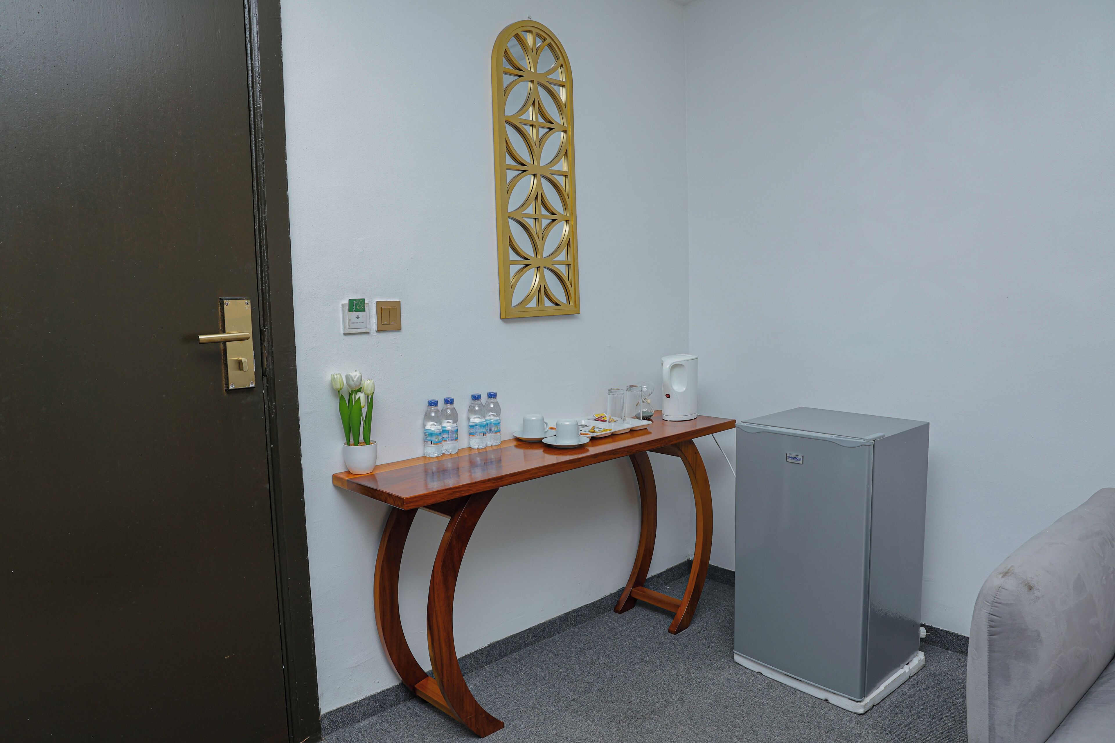Um quarto com uma mesa de madeira, um refrigerador, um ornamento de parede e uma porta.