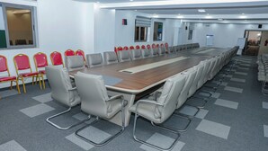 A conference room with a long table, multiple chairs, and a carpeted floor. - Les jardins d'Adzopé (Adzope)
