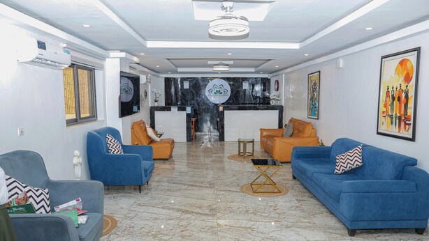 A modern hotel lobby with a reception desk, seating area with sofas and chairs, a marble floor, and artwork on the walls. - Les jardins d'Adzopé (Adzope)