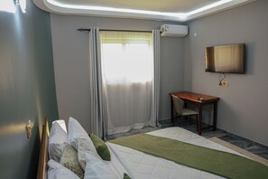 Habitación de hotel con cama, escritorio, silla, televisor y aire acondicionado.