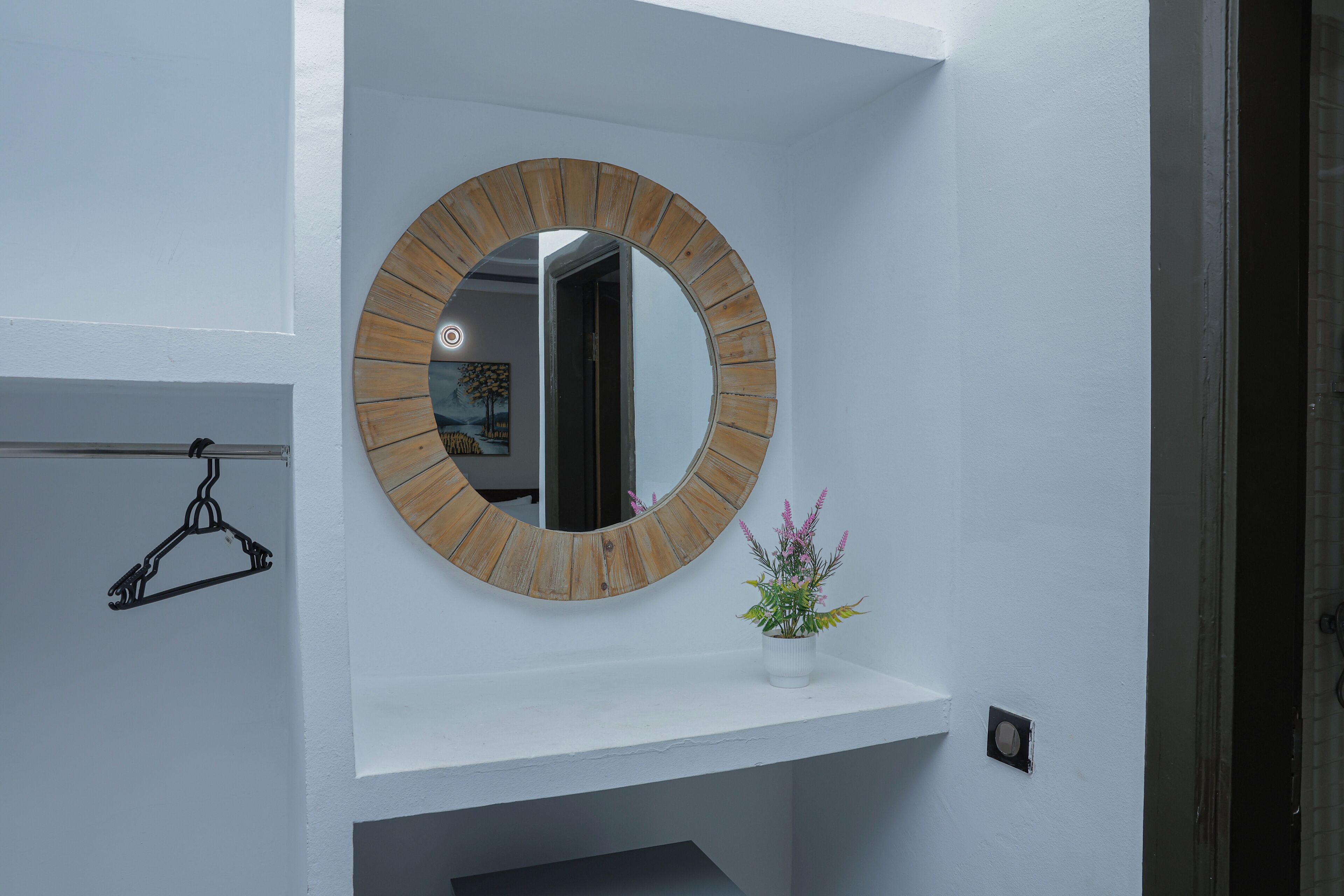 Une salle de bain avec un miroir rond, un porte-serviettes et une petite plante en pot.