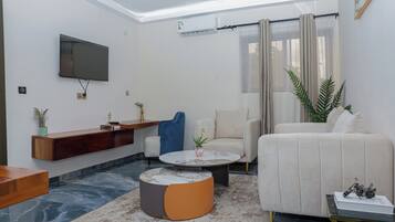 Un salon moderne avec un téléviseur à écran plat fixé au mur, un canapé, une table basse et une petite table d’appoint.