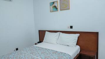 Habitación de hotel con cama, mesita de noche, aire acondicionado instalado en la pared y dos obras de arte enmarcadas.