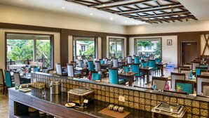 A spacious dining area with multiple tables and chairs, a buffet counter, and large windows offering views of greenery.