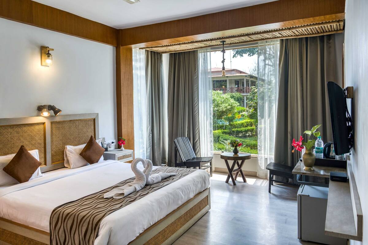 Habitación de hotel con cama, escritorio, silla, televisor y vista a áreas verdes.
