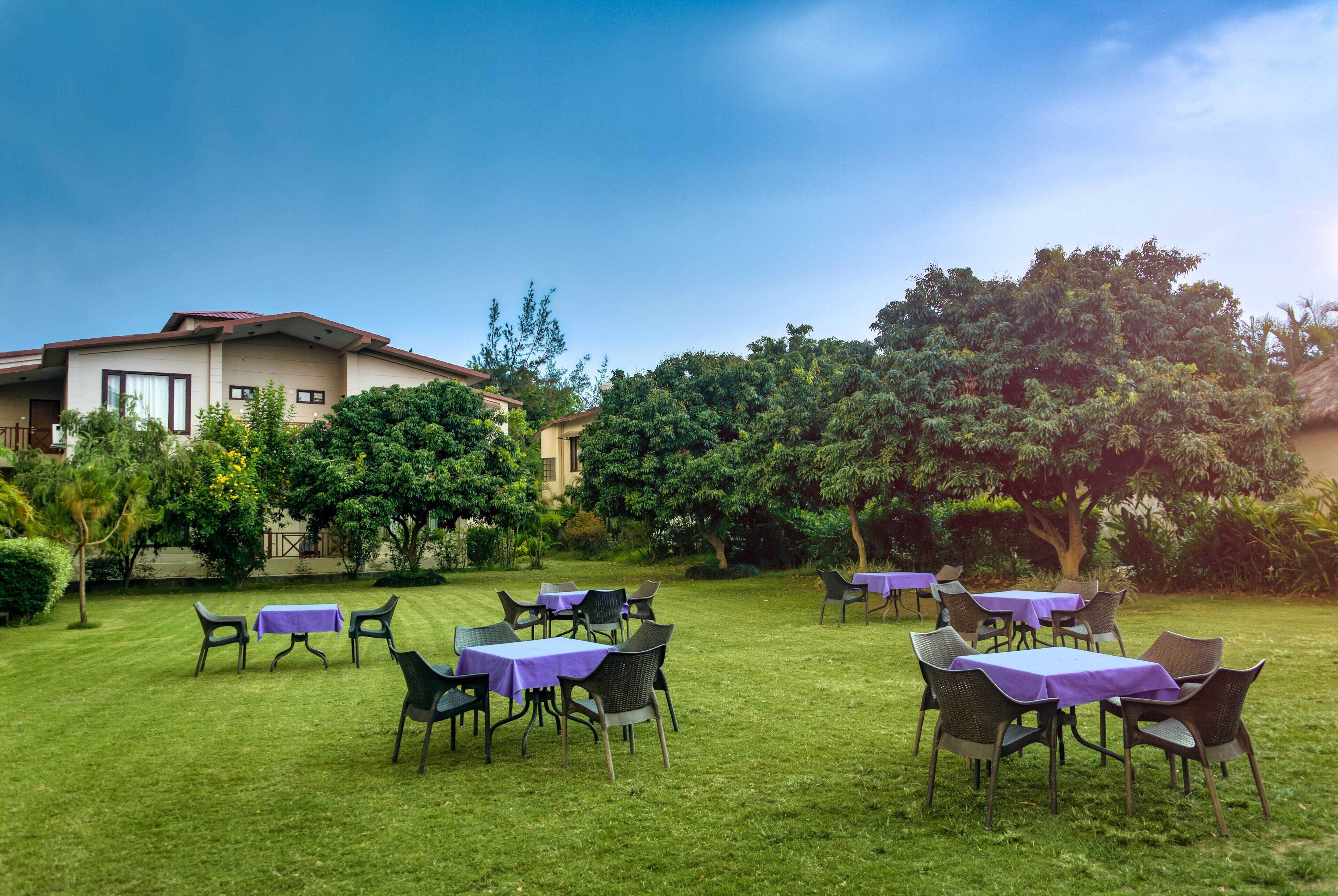 A garden with tables and chairs, a building in the background, and trees.