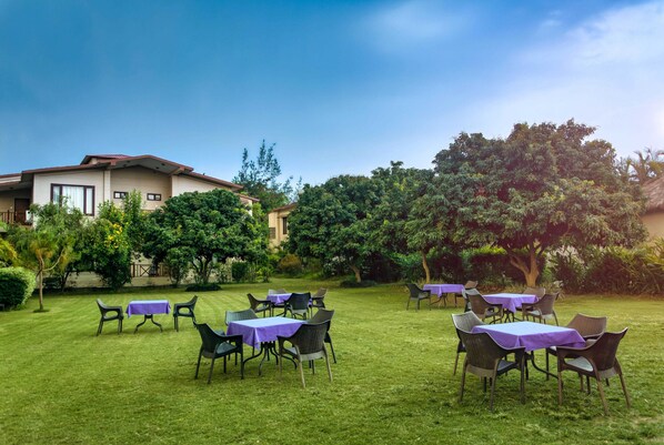 A garden with tables and chairs, a building in the background, and trees.