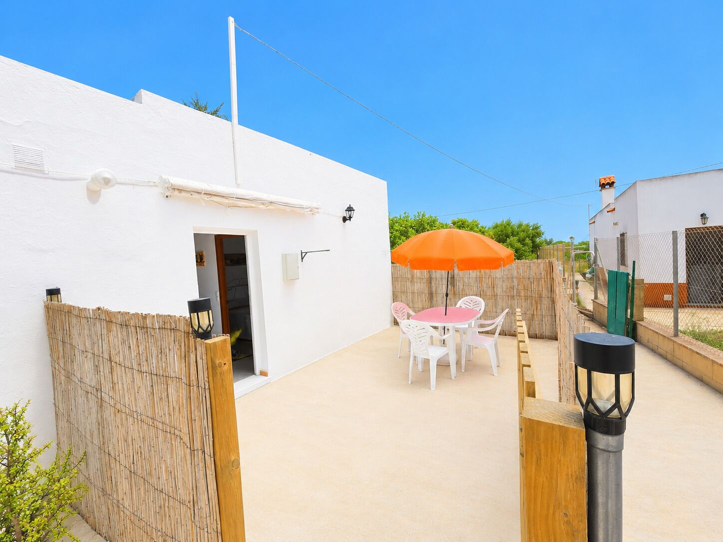 A white building with a door, a table with chairs, and an orange umbrella.