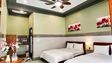 A hotel room with two beds, a ceiling fan, a dining table with chairs, and artwork on the walls.