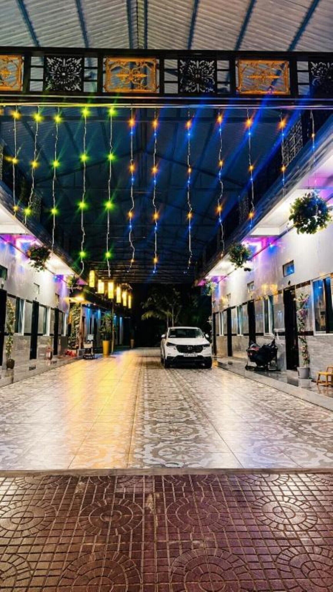 Un paseo techado con luces colgantes, un coche estacionado en el centro y macetas con plantas a lo largo de los lados.