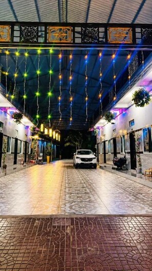 A covered walkway with hanging lights, a car parked in the center, and potted plants along the sides. - Tien Phat Hotel (Hoai Nhon Nam)