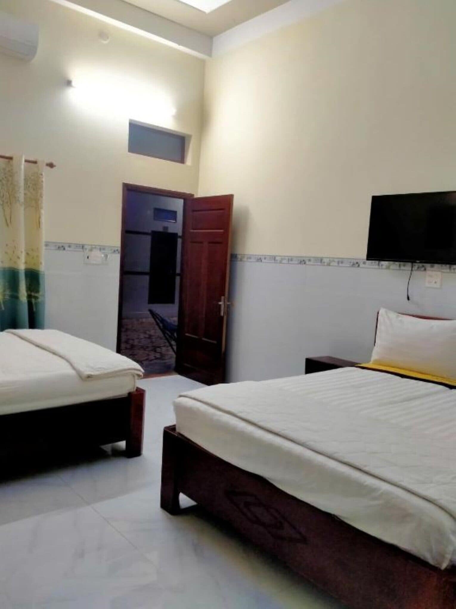 Habitación de hotel con dos camas, un televisor montado en la pared y una puerta que da a un balcón.