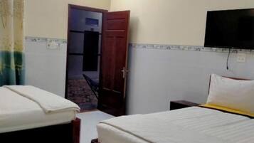 Habitación de hotel con dos camas, un televisor montado en la pared y una puerta que da a un balcón.
