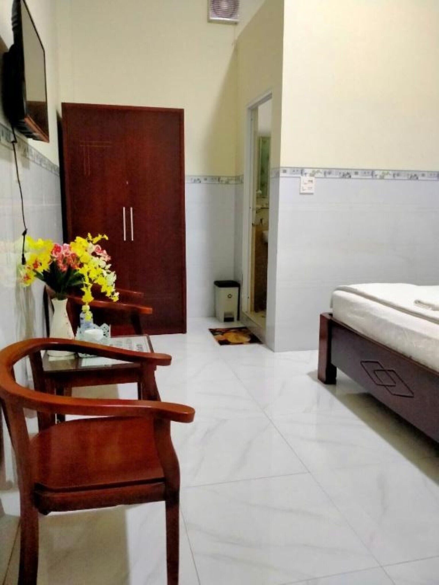 A hotel room with a wooden desk, chairs, a bed, and a small table with a vase of flowers.