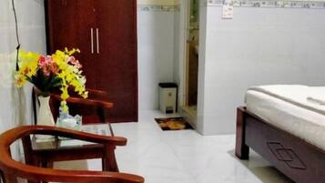 A hotel room with a wooden desk, chairs, a bed, and a small table with a vase of flowers.
