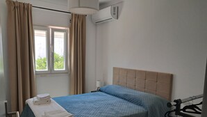 A single bed with a blue quilt, a wooden headboard, and a window with curtains.
