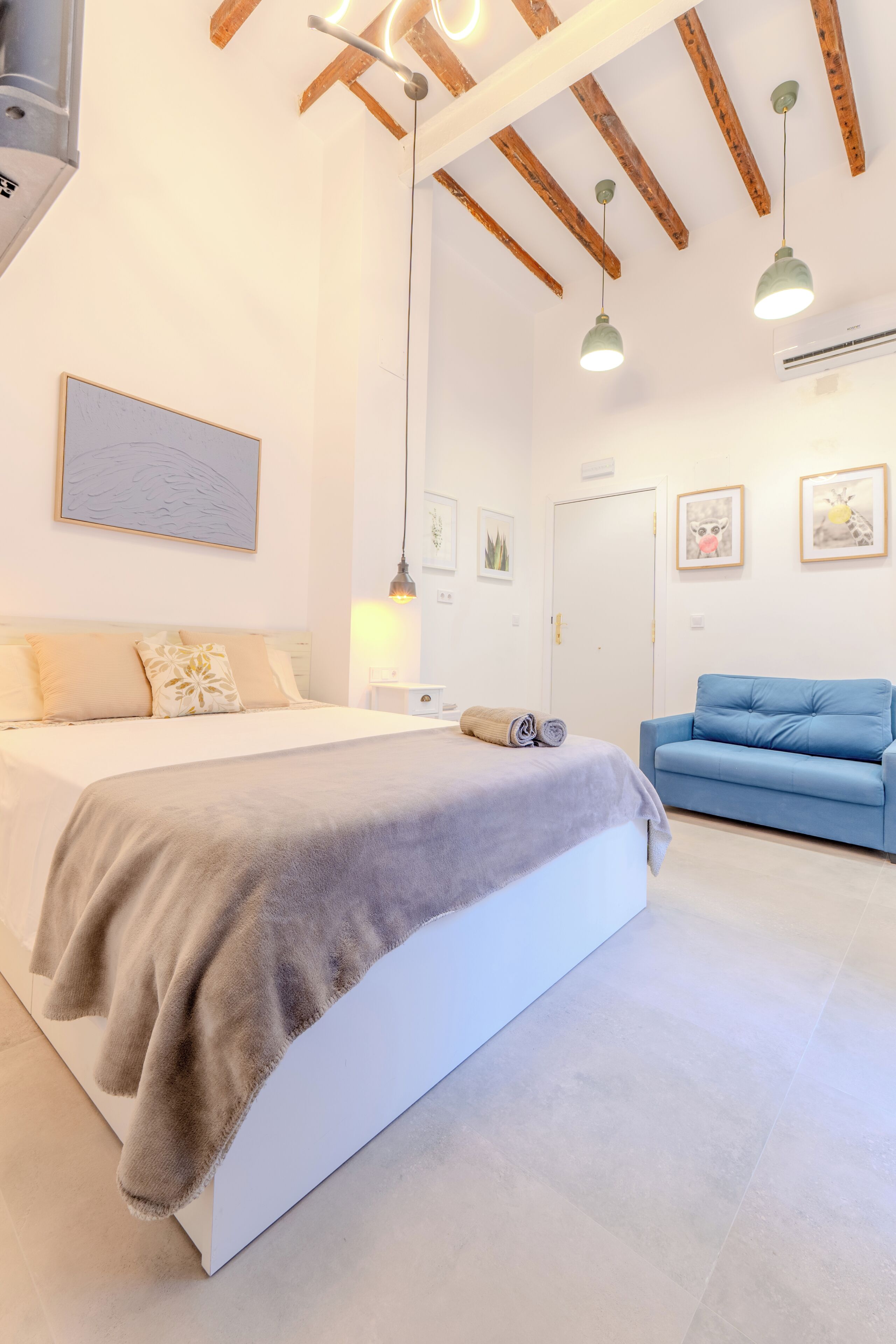 A bedroom with a bed, a blue sofa, a ceiling fan, and a wall-mounted air conditioner.