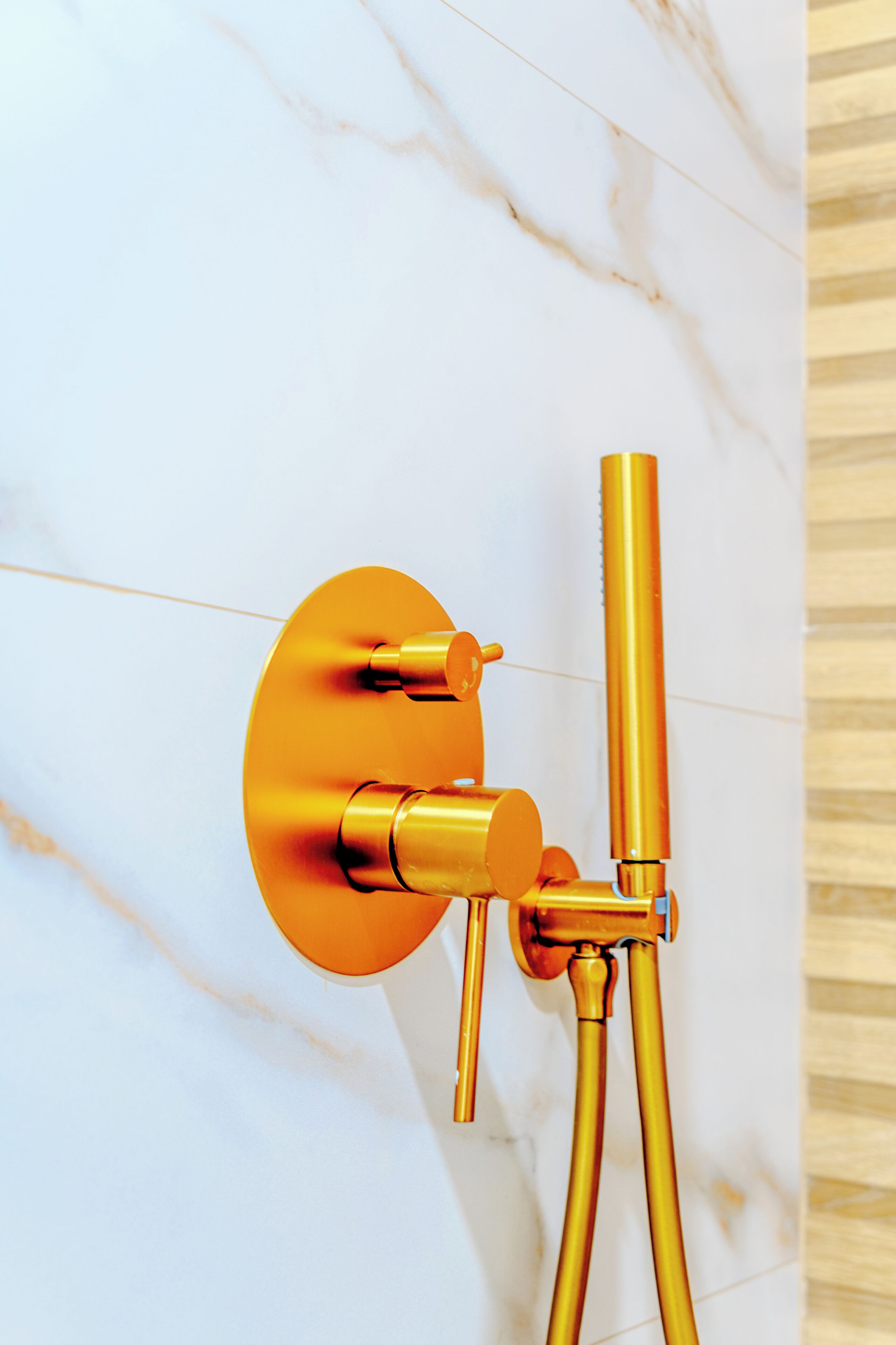 Een badkamer met een marmeren wand, een gouden douchekop en een gouden kraan.