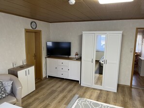 Ett rum med en tv-apparat placerad på ett träskåp, en soffa, en garderob och en dörr som leder till ett annat rum.