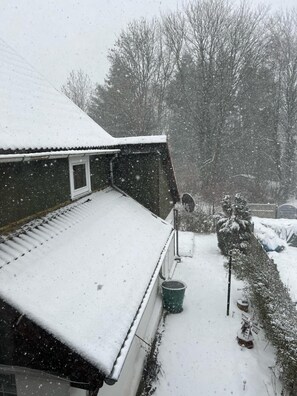 En bostadsbyggnad med ett sluttande tak, ett väl synligt fönster och en snötäckt gård.