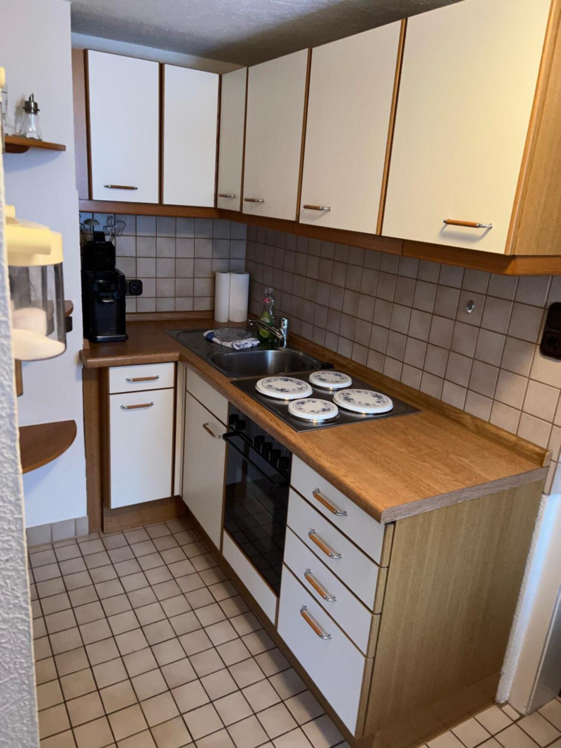 Et lille køkken med hvide skabe, kaffemaskine, vask og komfur.