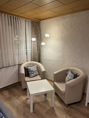 Ett modernt rum med två beige fåtöljer, ett vitt bord, ett träpanelat tak och ett element.