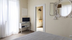 A bedroom with a bed, a dresser with a TV, a mirror, and a door leading to a bathroom. - Relais Bellavista, Tuscany (suvereto)