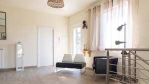 A spacious room with a wooden floor, a white door, a bench, two chairs, a staircase, and a hanging light fixture. - Relais Bellavista, Tuscany (suvereto)