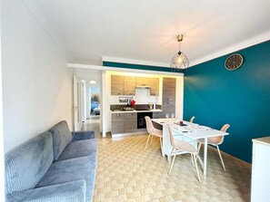 A modern living room with a sofa, a dining area with a table and chairs, and a kitchen in the background.