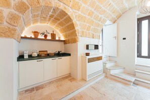 A kitchen with white cabinets, a stone arch, a wooden countertop, and a staircase leading to a landing. - Casa Volta Nova – Historic Hideaway (Polignano a Mare)