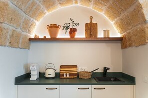 A kitchen with a brick arch, a coffee machine, a kettle, a cutting board, and a sink. - Casa Volta Nova – Historic Hideaway (Polignano a Mare)