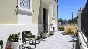 Un patio con mesas al aire libre, plantas en macetas y un edificio con contraventanas.