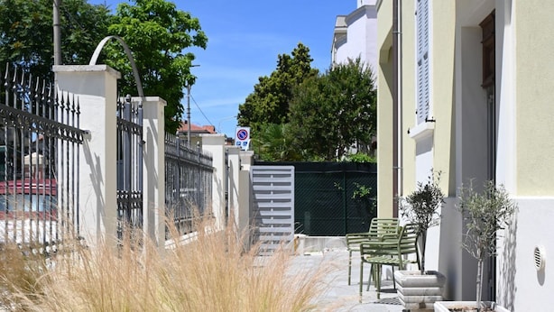 Una calle estrecha con una entrada porticada, un banco y plantas en macetas.