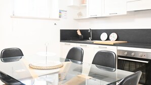 Una cocina moderna con armarios blancos, encimera negra, mesa de comedor de cristal y sillas negras.