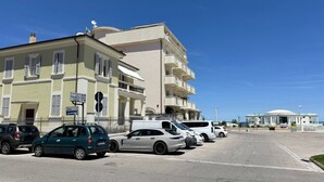 Un estacionamiento con varios autos, un edificio con múltiples balcones y un cielo azul despejado.