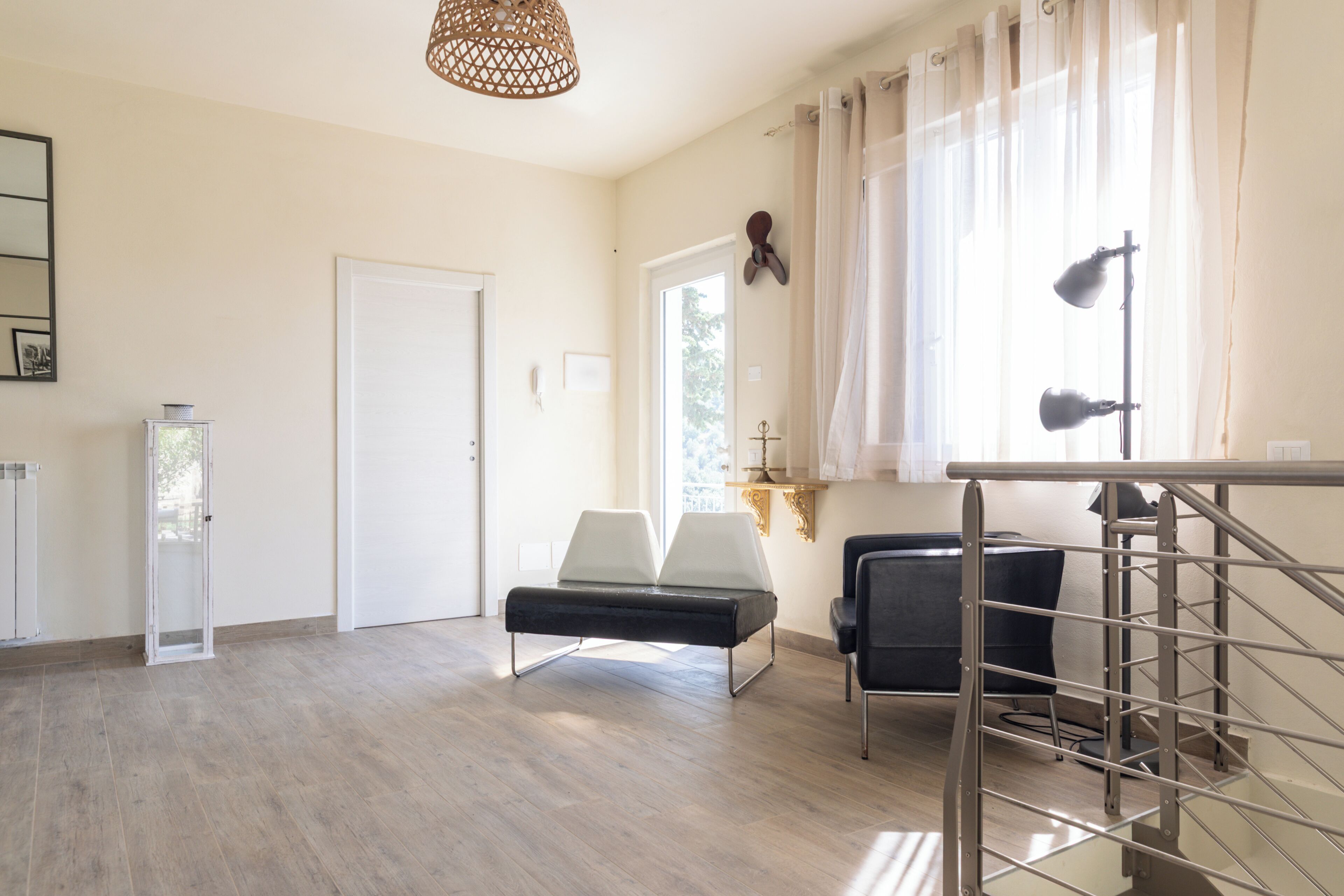 Une pièce avec un plancher en bois, un banc, une chaise, un bureau, une lampe et une fenêtre avec des rideaux.