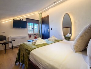 Una camera d'albergo con un letto, una sedia, una scrivania, una televisione, uno specchio e una finestra con vista.
