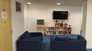 Une pièce avec deux canapés sombres, une bibliothèque, un téléviseur et une porte sur laquelle est apposée une pancarte.