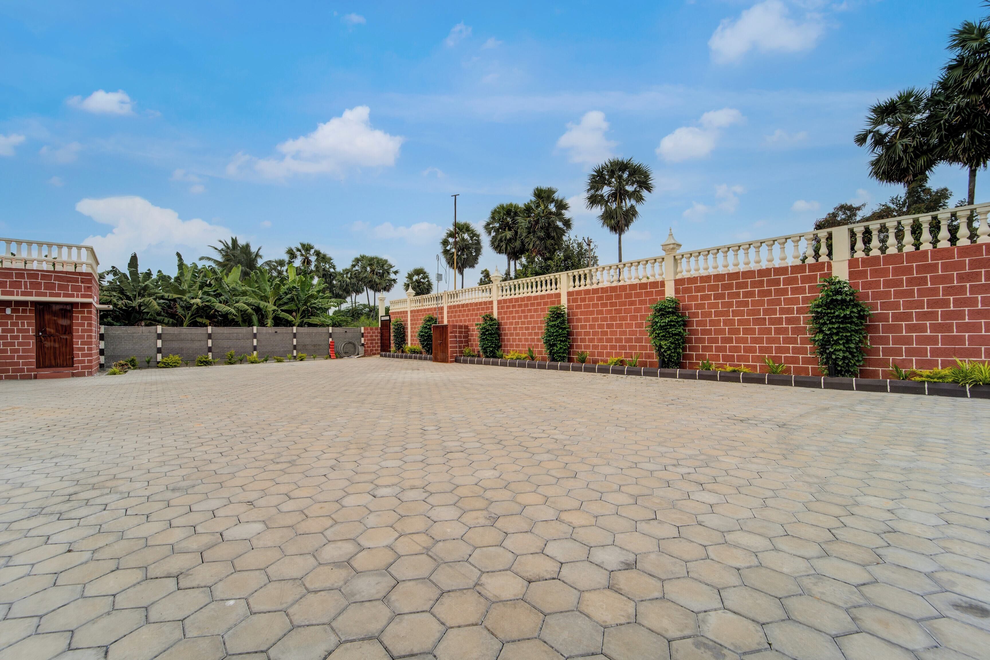 A spacious paved area with a brick wall and a decorative railing, surrounded by greenery and palm trees.