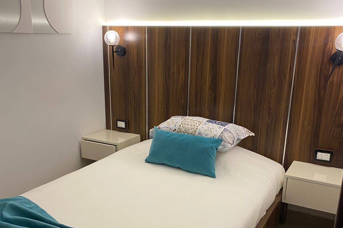 A neatly made bed with a teal throw, two bedside tables, and a wall-mounted light fixture.