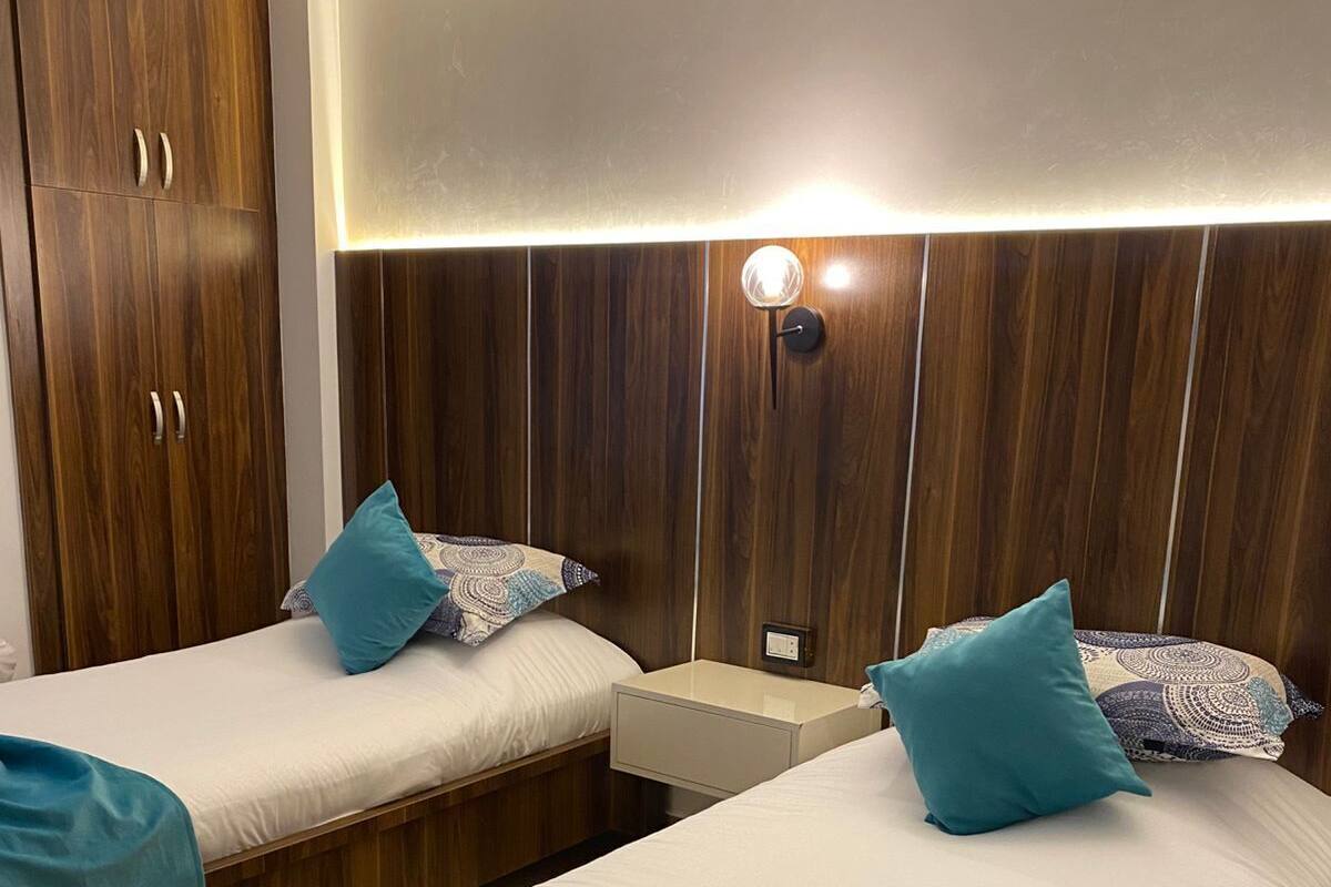 A hotel room with two beds, wooden wardrobe, bedside tables, and a wall-mounted light fixture.
