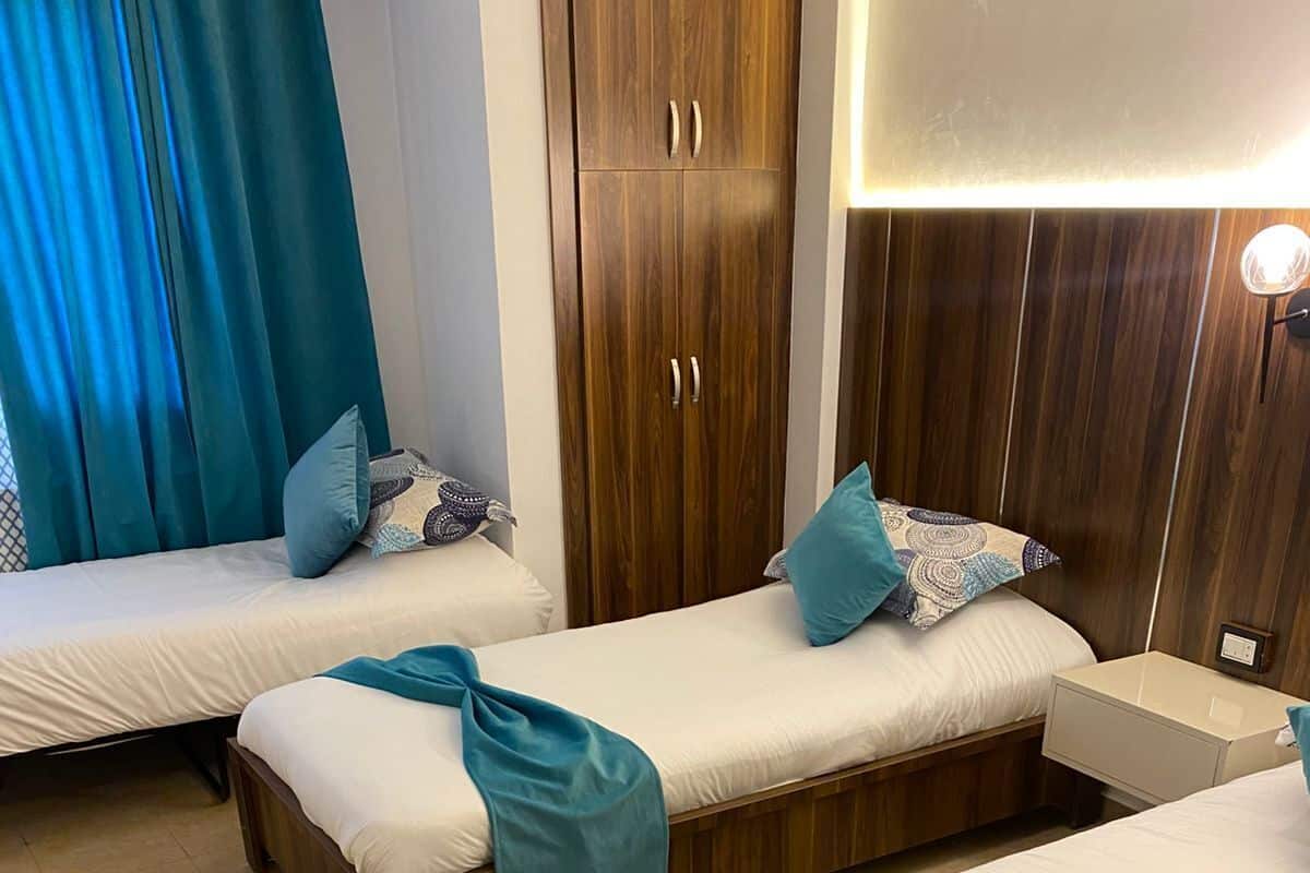 A hotel room with two single beds, wooden headboards, a nightstand, and a wardrobe.