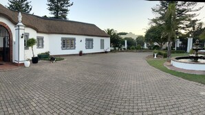 Un edificio blanco con techo de paja, dos coches aparcados y un camino de entrada pavimentado.