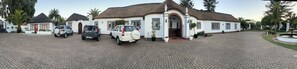 A white building with a thatched roof, two parked cars, and a paved driveway.