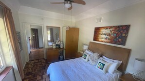 Habitación de hotel con cama, ventilador de techo, un cuadro, microondas y puerta que da a otra habitación.