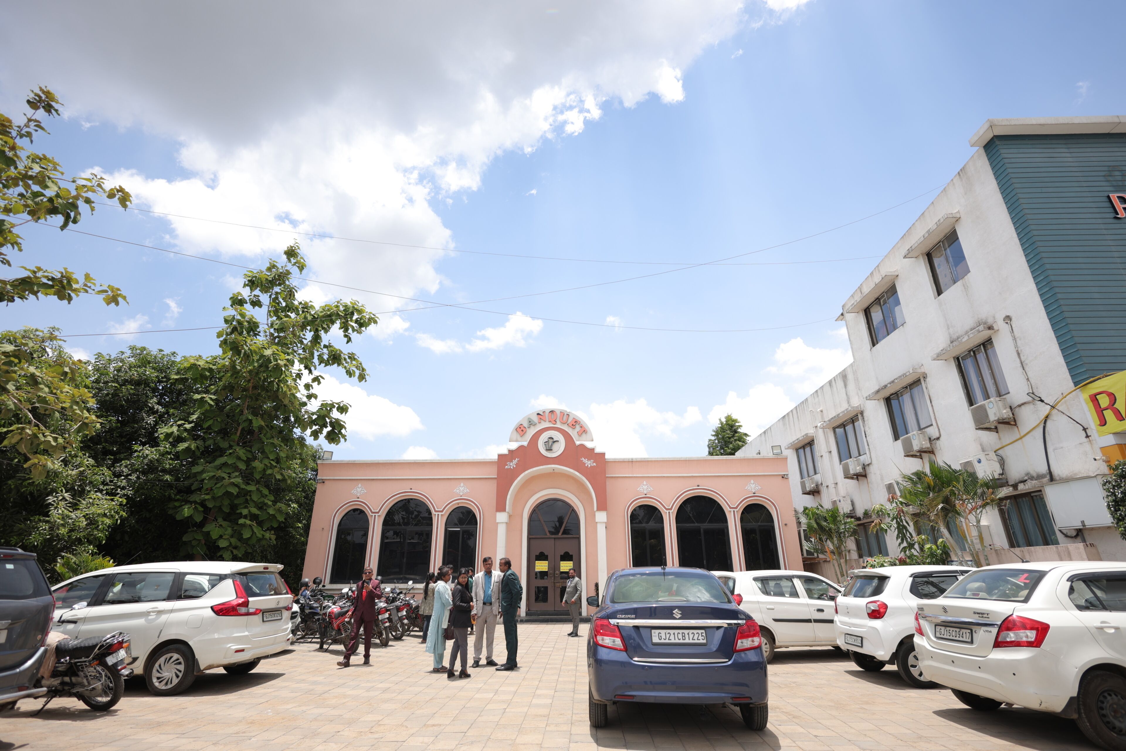 A building with a central arched entrance, multiple windows, and parked cars in front.